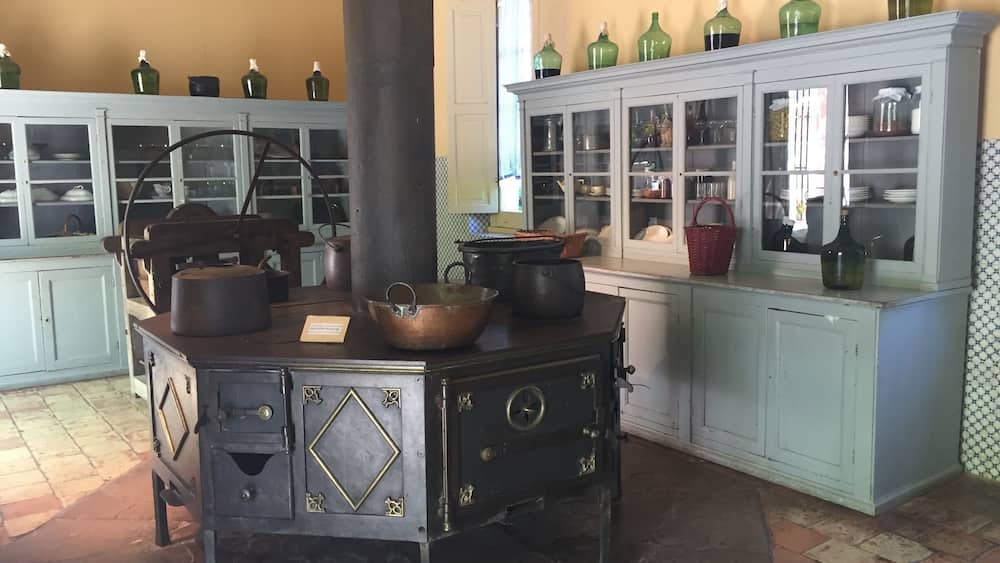 A vintage kitchen with a stove, copper pots, and glass cabinets filled with dishes.