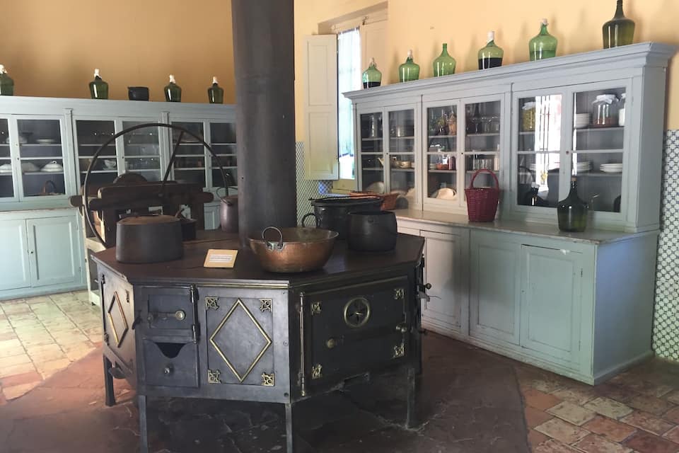 Une cuisine d’époque avec un poêle, des casseroles en cuivre et des meubles vitrés remplis de vaisselle.