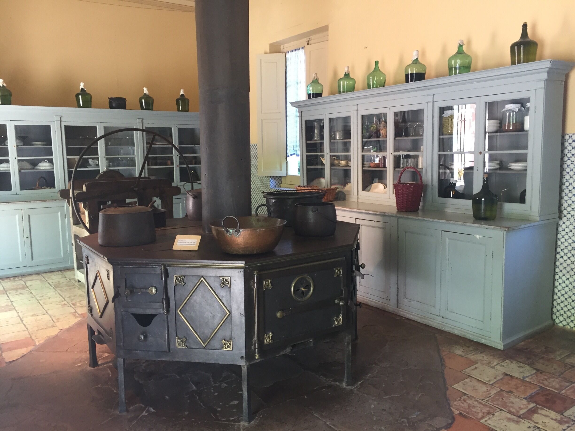 A vintage kitchen with a stove, copper pots, and glass cabinets filled with dishes.
