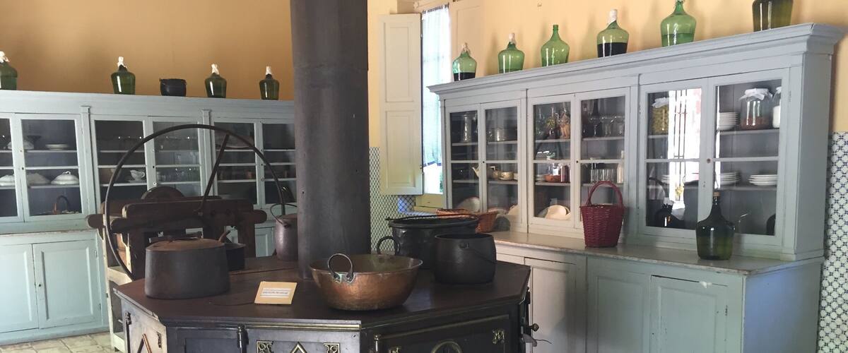 A vintage kitchen with a stove, copper pots, and glass cabinets filled with dishes.