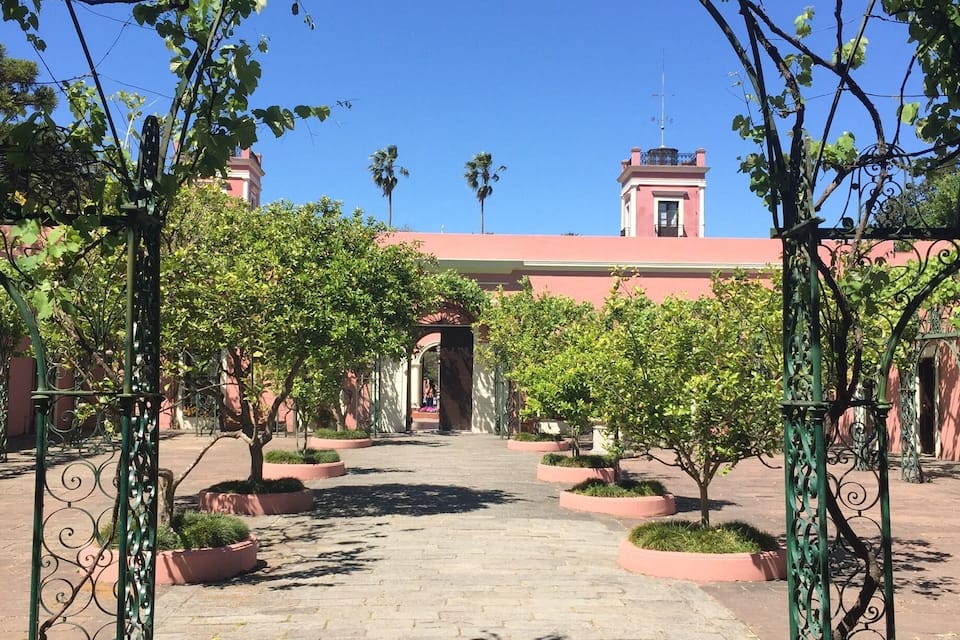 A pathway lined with trees and a wrought iron archway leading to a building with a red facade.