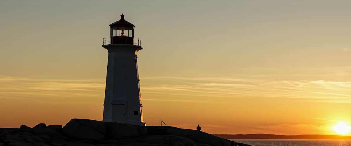 A lighthouse at sunset with a clear sky and calm sea.