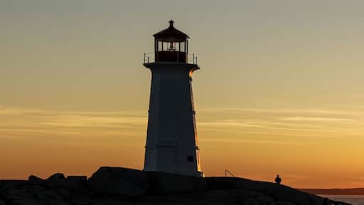 A lighthouse at sunset with a clear sky and calm sea.