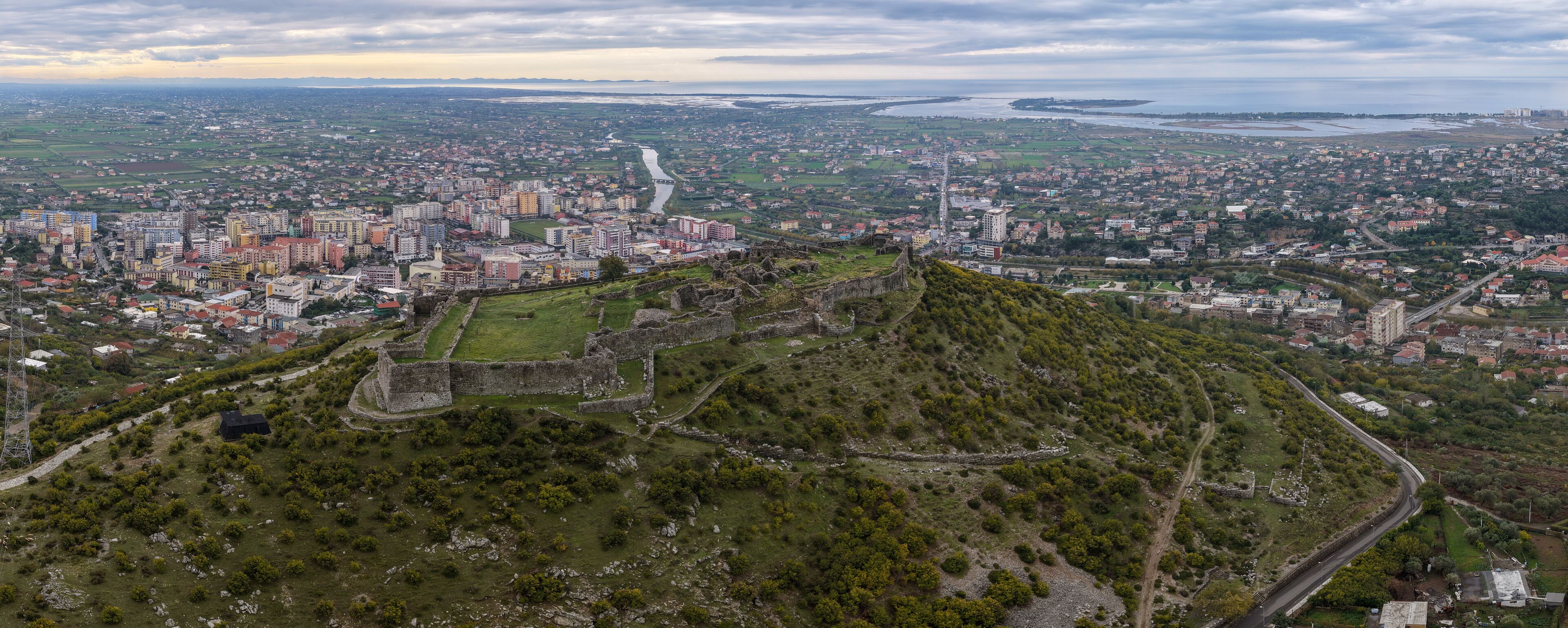 Aerial panorama of Lezhë Castle overlooking the town, Drin River and the Adriatic wetlands under soft cloudy evening light.