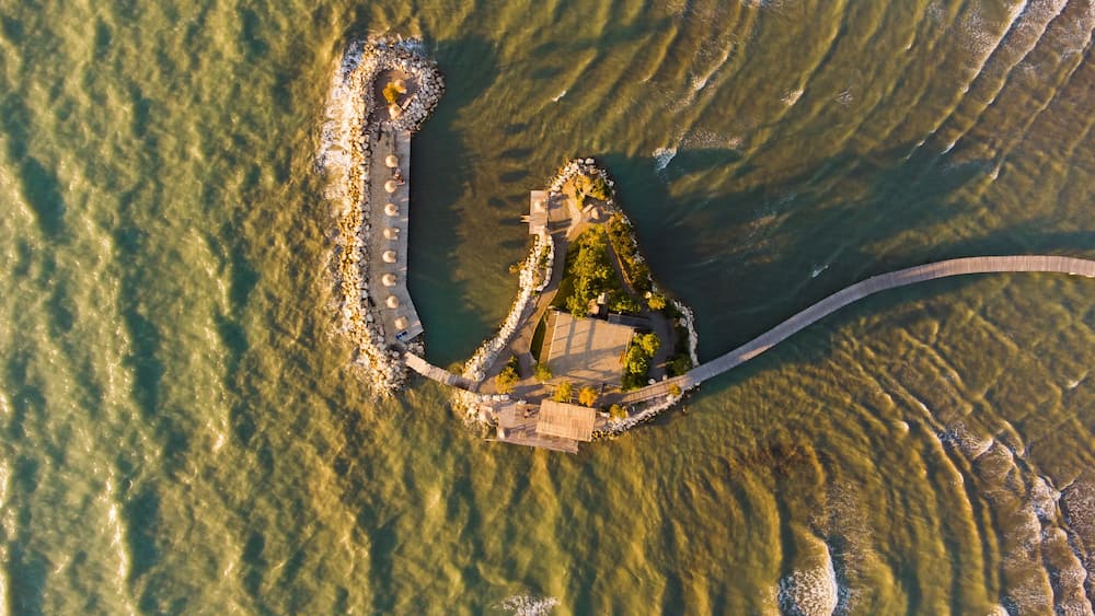 An aerial view of a coastal area with a long pier extending into the water, surrounded by rocks and greenery.