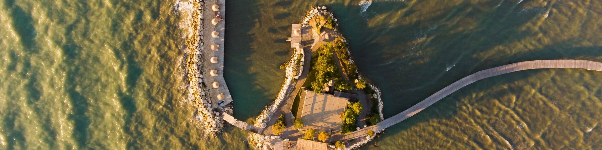 An aerial view of a coastal area with a long pier extending into the water, surrounded by rocks and greenery.
