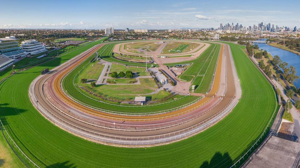 A large racetrack with multiple lanes, surrounded by green fields and a river.