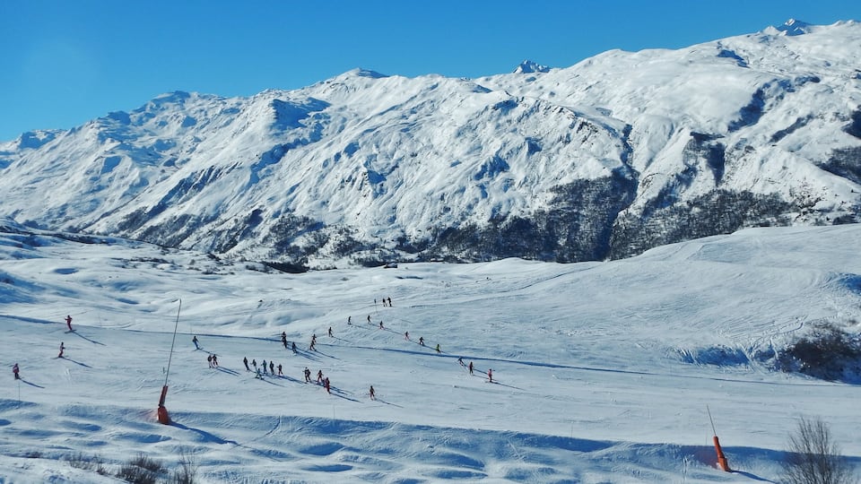 A snowy mountain slope with skiers and a clear blue sky.