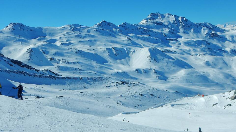A snowy mountain landscape with skiers and a ski lift.