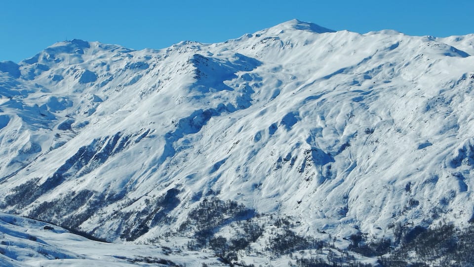 A snow-covered mountain with rugged terrain and sparse vegetation.