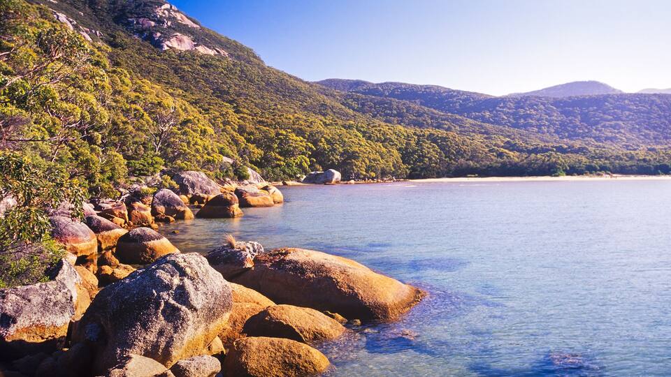 A coastal landscape with large rocks, clear water, and green hills.