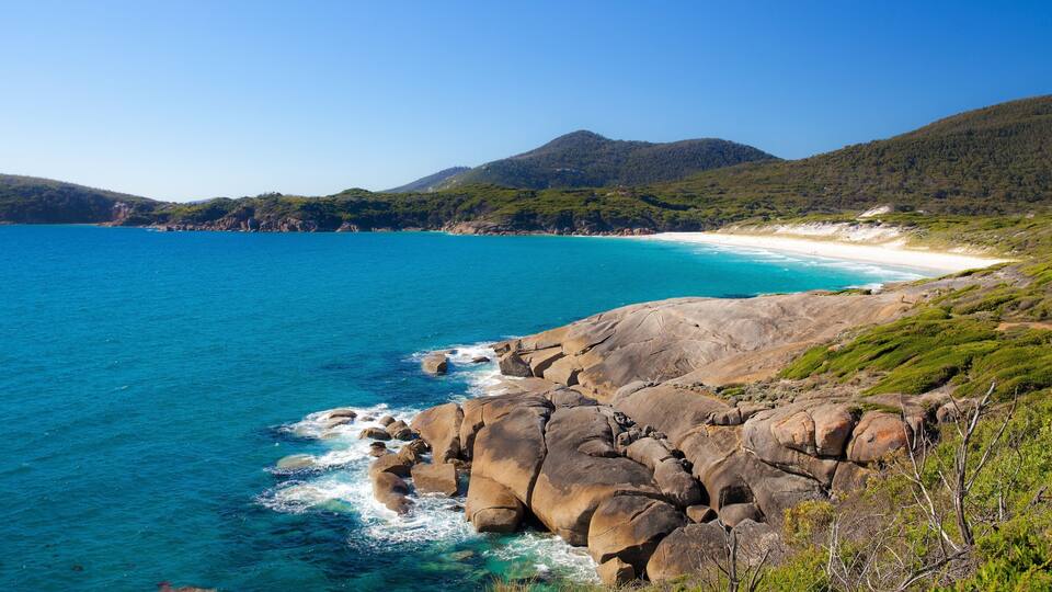 A coastal landscape with a rocky shoreline, clear blue sea, and a sandy beach.