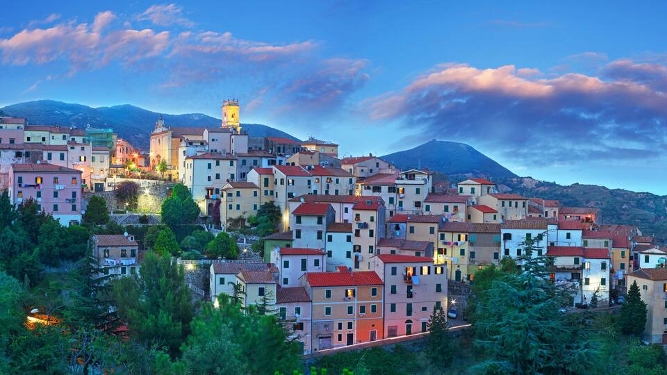 A hillside town with colorful buildings, a prominent tower, and a mountain in the background.