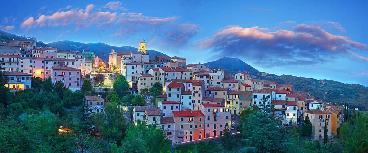 A hillside town with colorful buildings, a prominent tower, and a mountain in the background.
