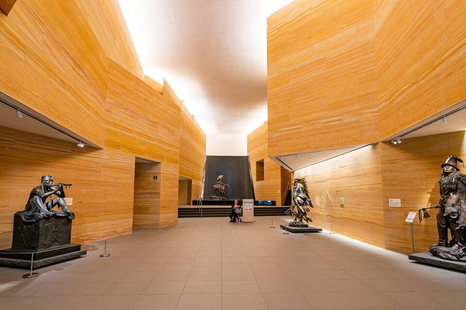 Interno di un museo con pareti in pannelli di legno, una scala centrale e tre sculture in bronzo.
