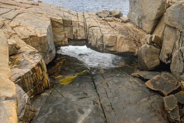 Un paysage côtier rocheux, avec un étroit passage d’eau entre de gros blocs de pierre.
