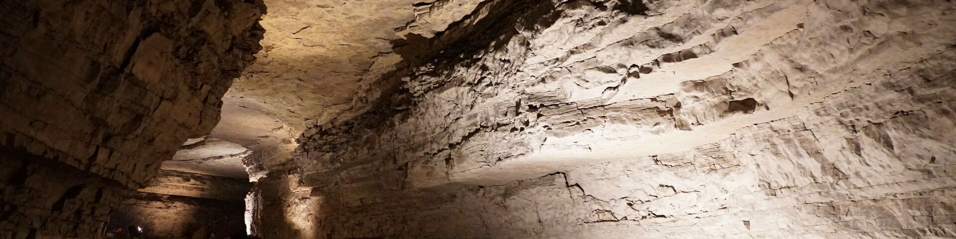 Uma gruta com um corredor estreito, paredes irregulares e ambiente pouco iluminado.