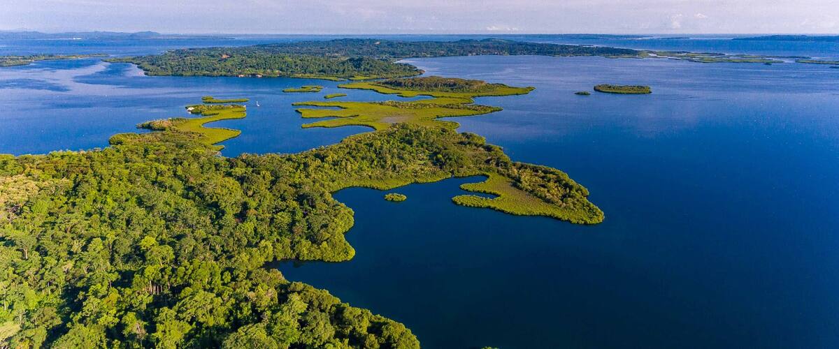 An aerial view of a coastal area with numerous small islands surrounded by water, dense green forests, and a distant shoreline.
