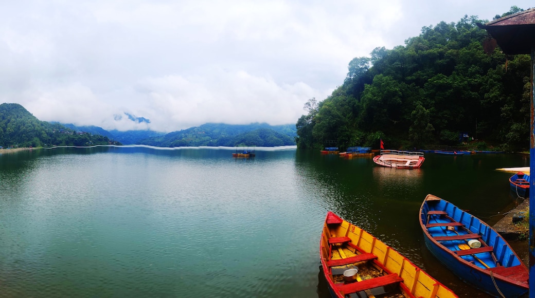 A calm river with boats, lush green hills, and a cloudy sky.