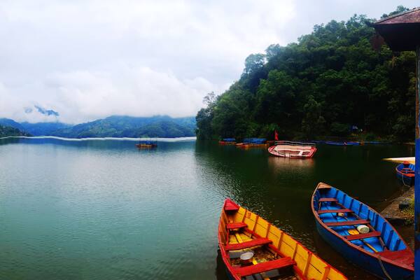 A calm river with boats, lush green hills, and a cloudy sky.