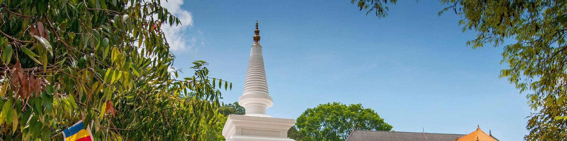 A white stupa with colorful stripes, surrounded by flags and a traditional building.