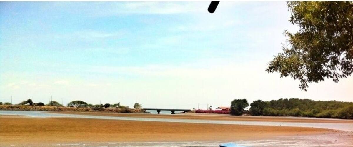 A beach with a boat, a bridge in the background, and trees.