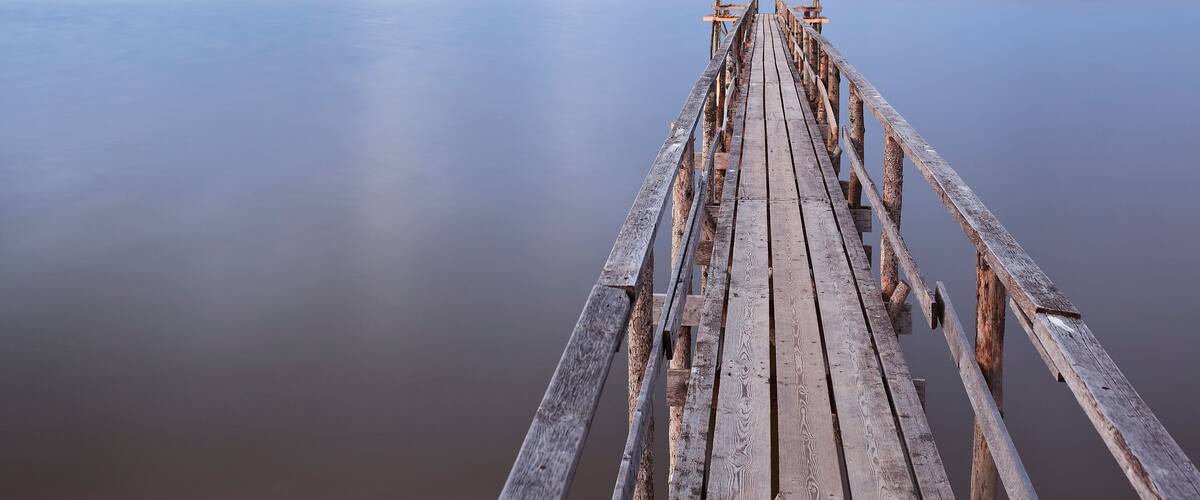 A wooden pier extending into calm water under a cloudy sky.