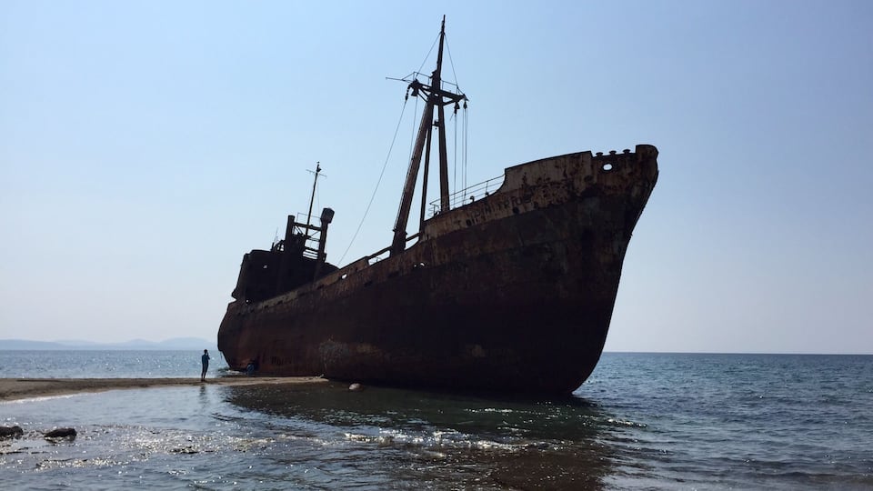 A large, rusted shipwreck stranded on a beach.