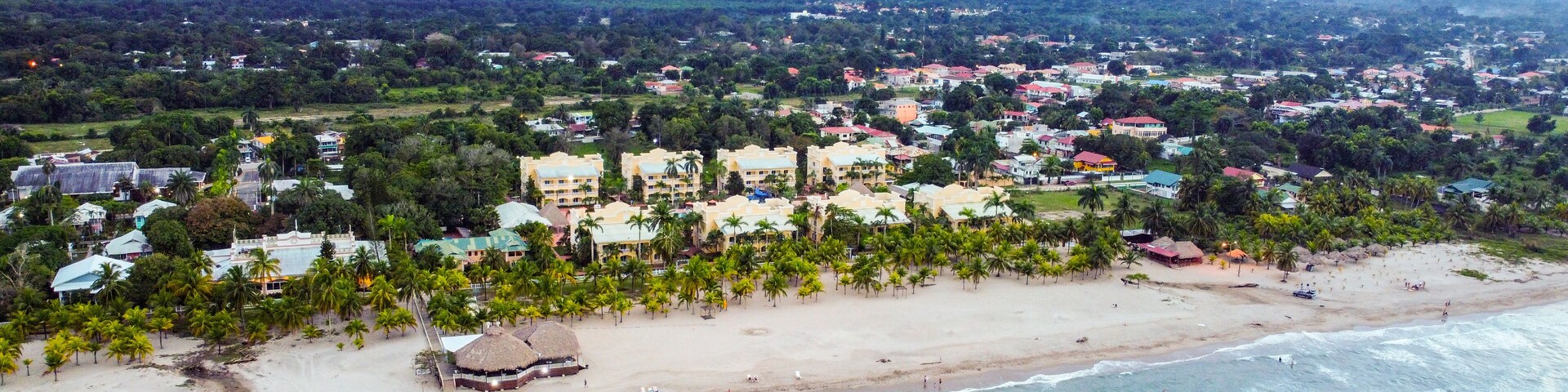 Un pueblo costero con playa, palmeras y montañas al fondo.