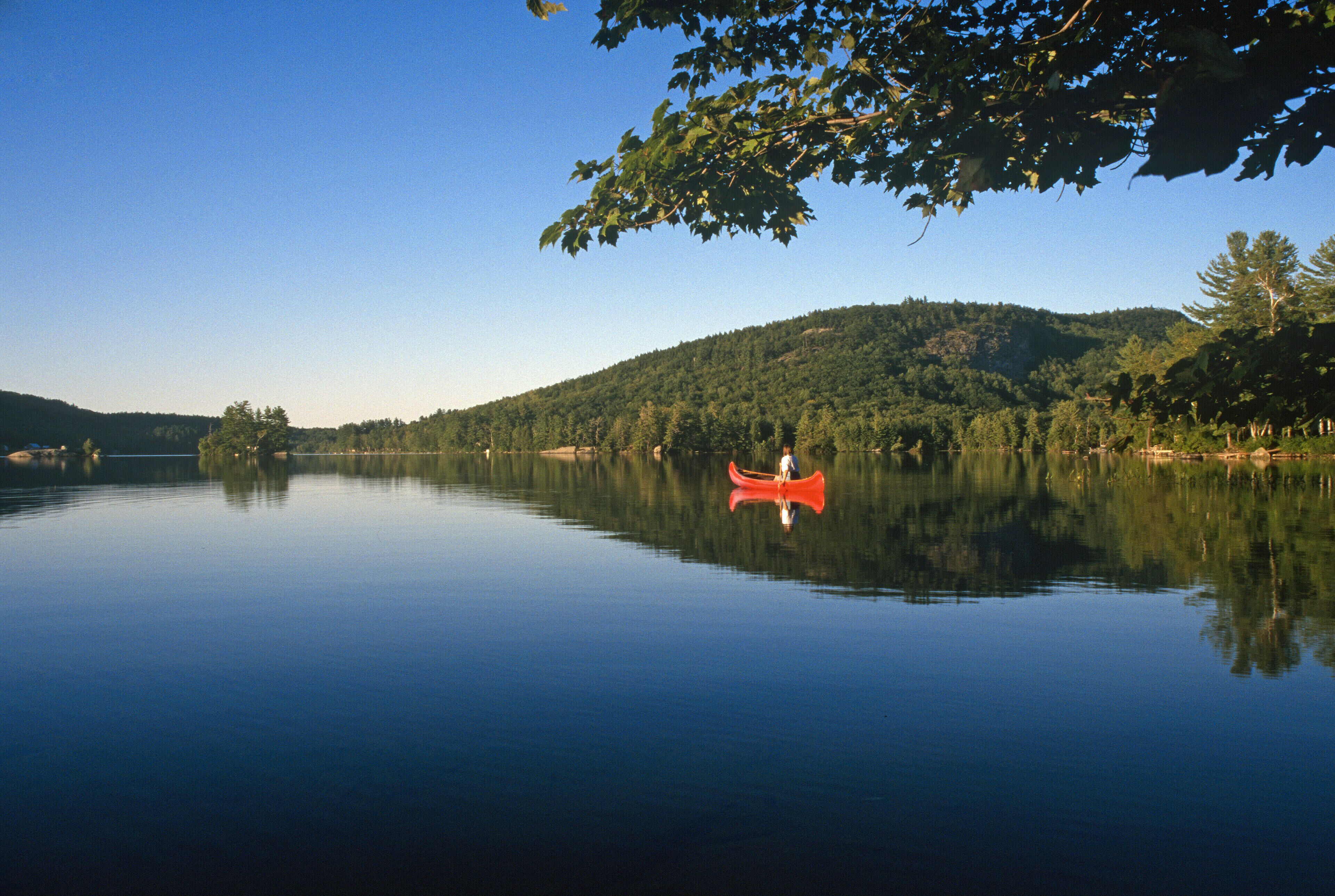 A calm lake with a red canoe, surrounded by dense forest and hills.