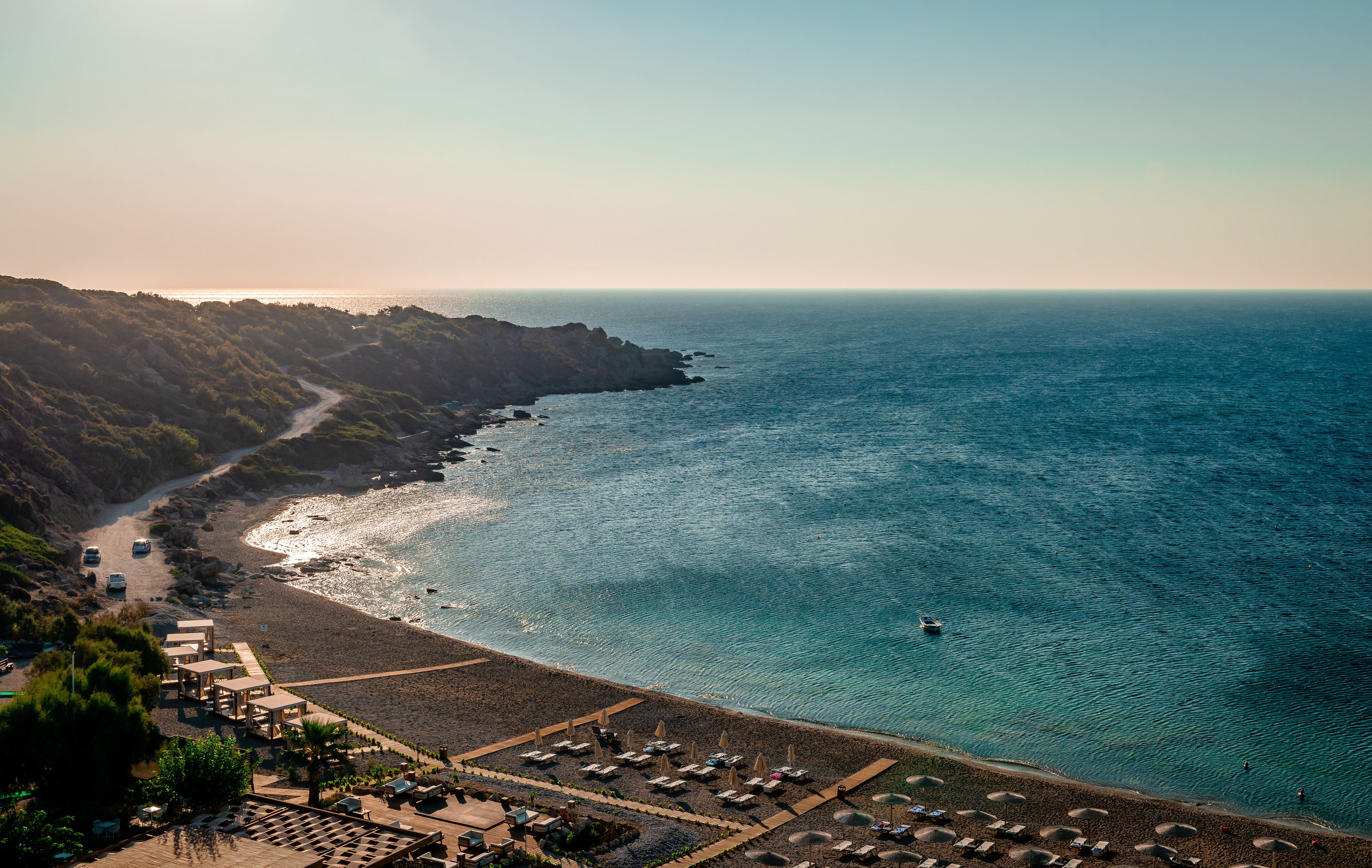 A coastal landscape with a beach, rocky cliffs, and a clear view of the ocean.