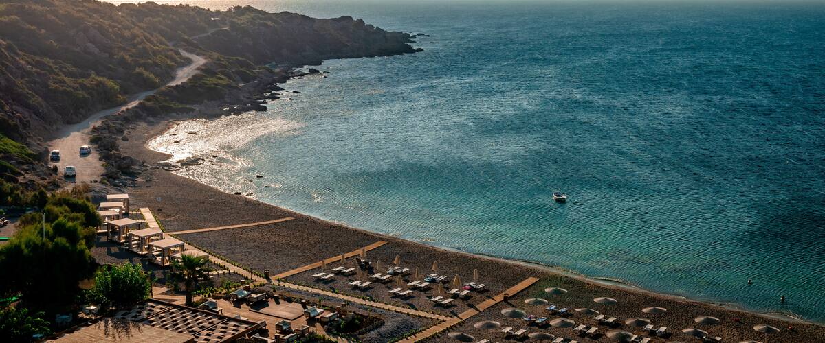 A coastal landscape with a beach, rocky cliffs, and a clear view of the ocean.