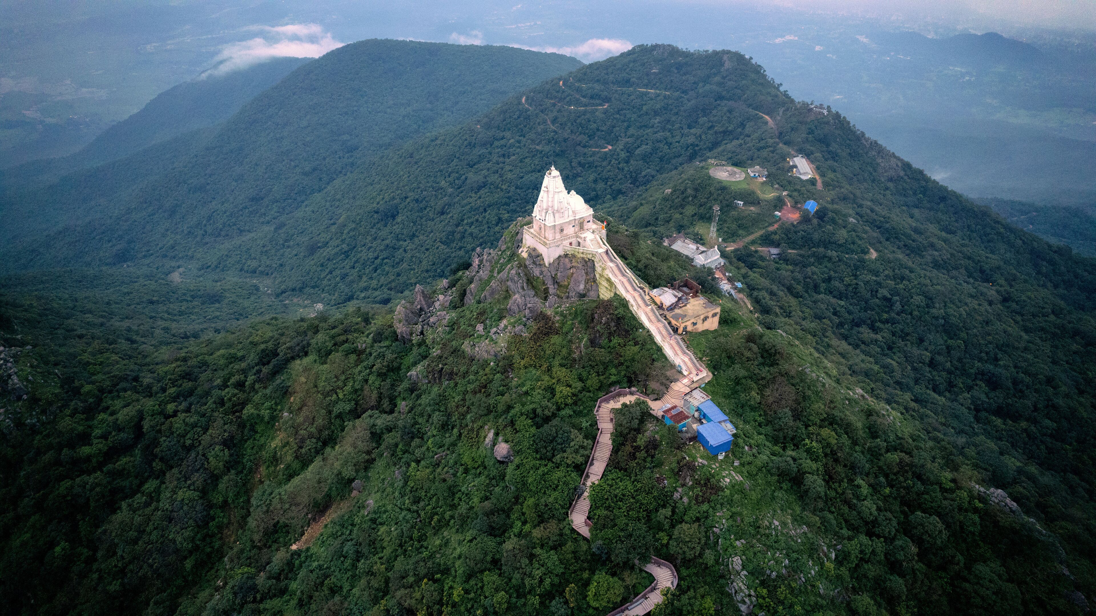 A temple on a mountain peak surrounded by dense forest.