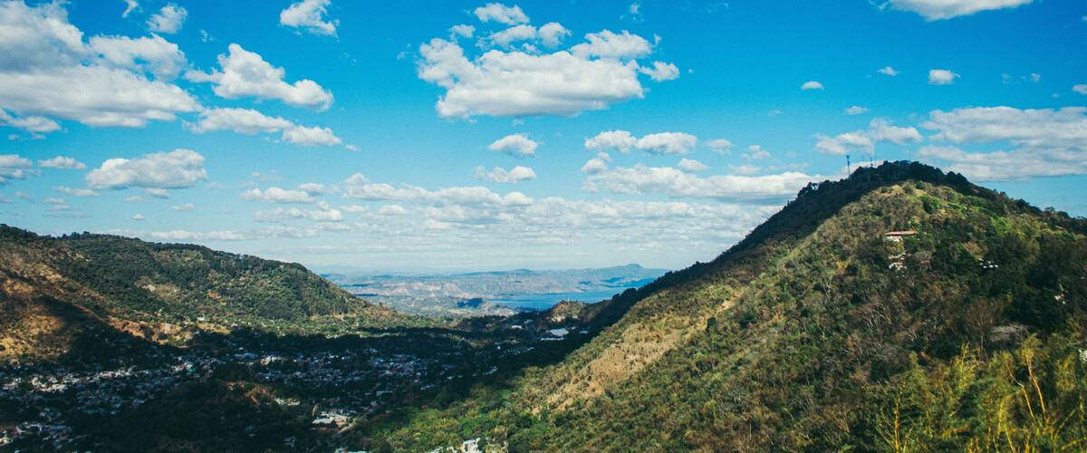 A valley with a mountain range, a river, and a distant cityscape.