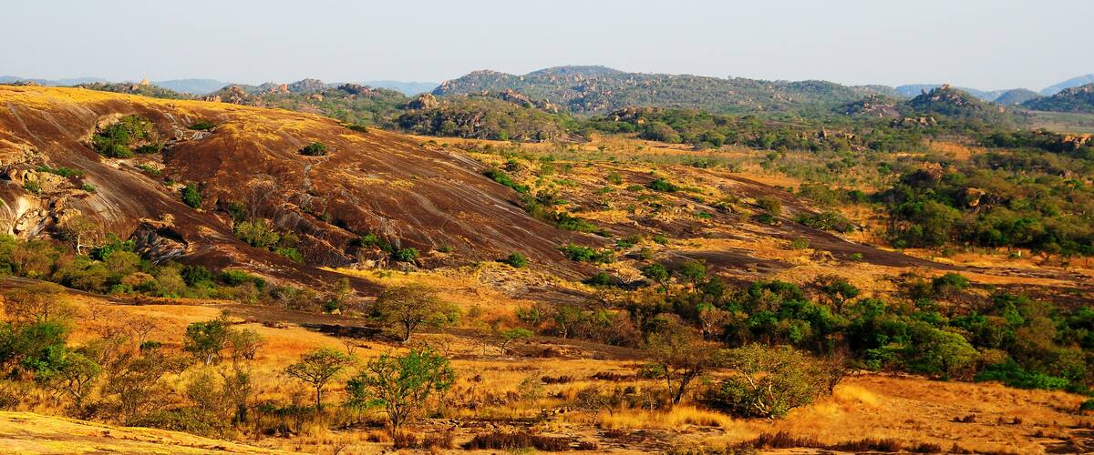 A dry, hilly landscape with sparse vegetation and distant hills under a clear sky.