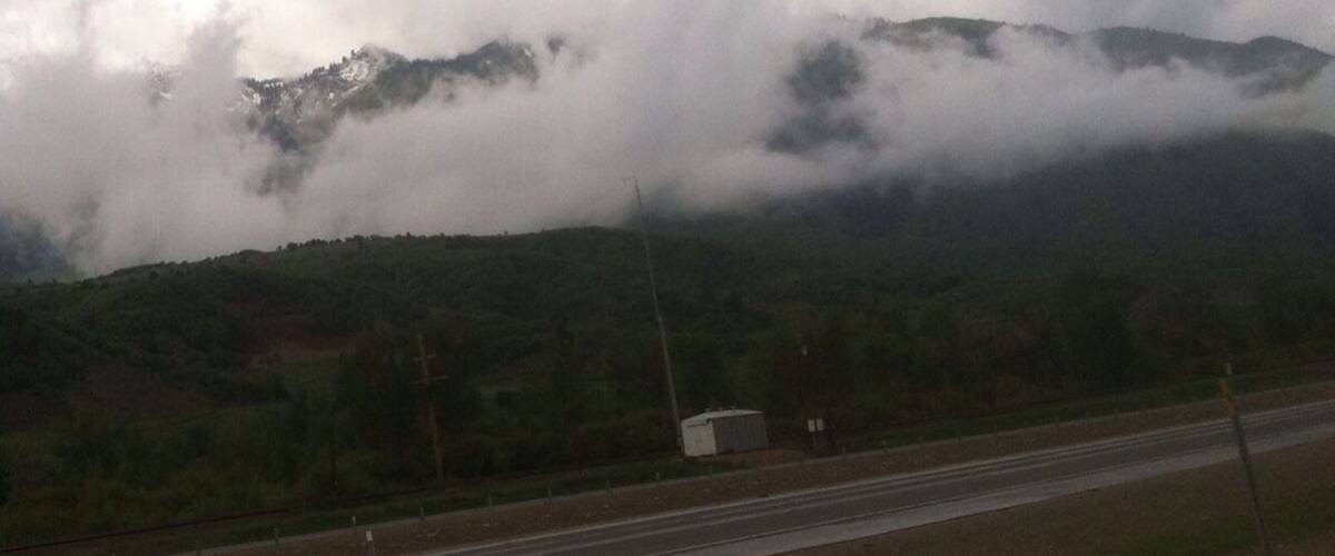 A highway with mountains in the background partially obscured by clouds.