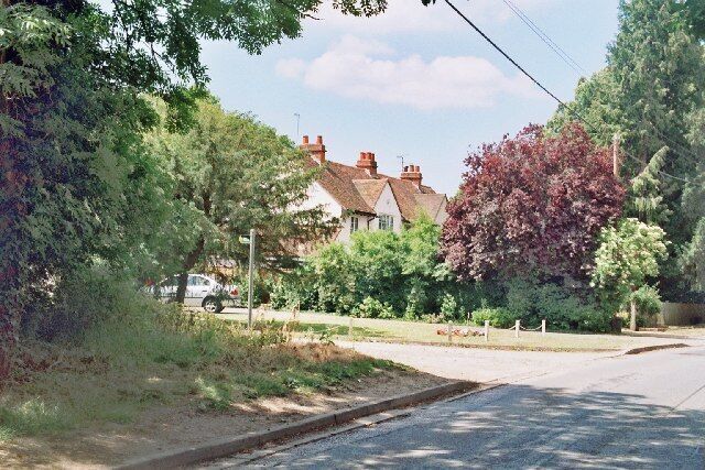 A quiet residential street with houses, trees, and a clear sky.