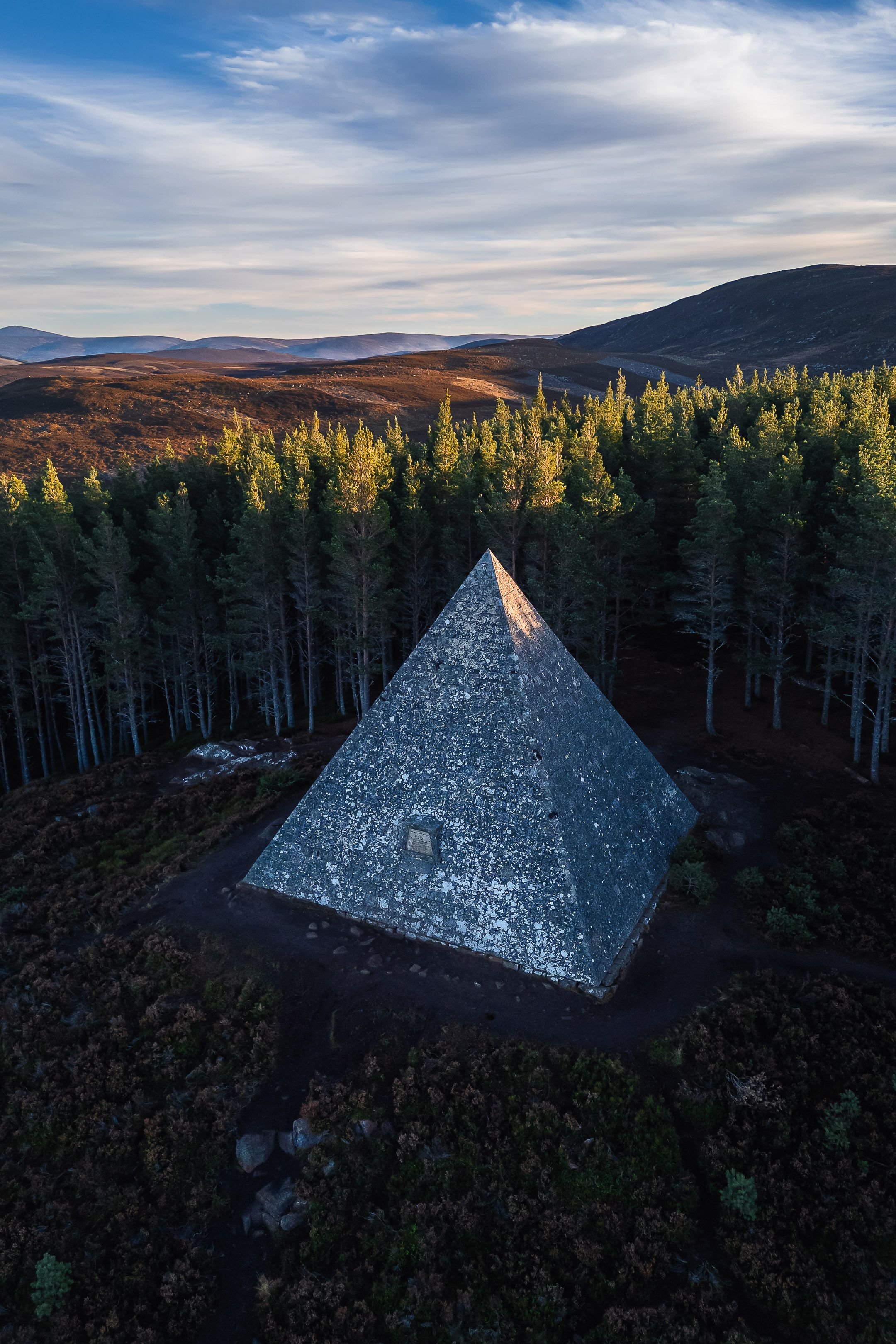 Una estructura piramidal rodeada por un bosque frondoso y montañas al fondo.