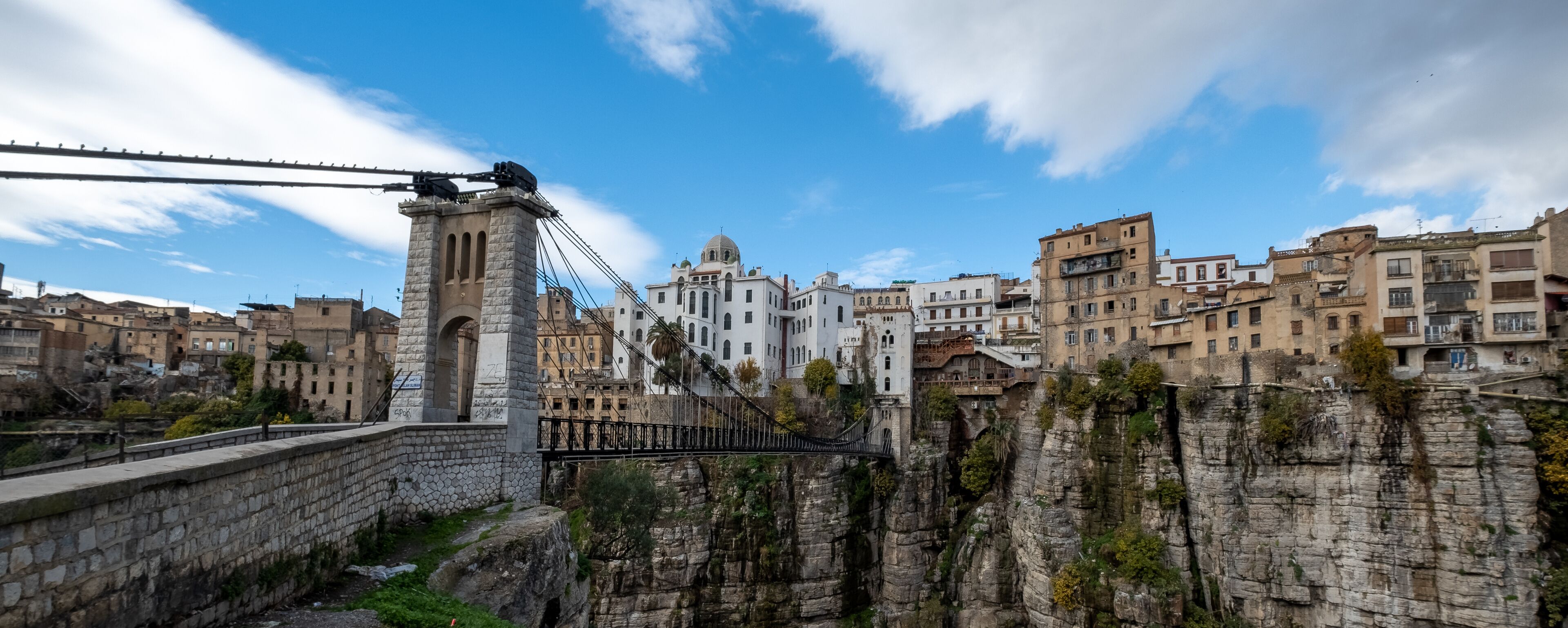 A stone bridge over a rocky gorge, a white church with a dome, and residential buildings.