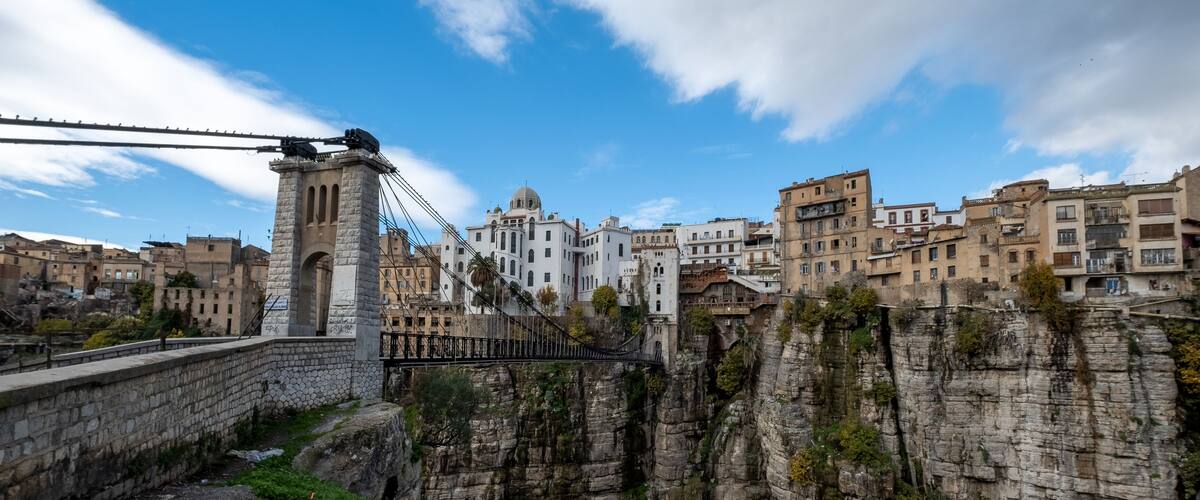 A stone bridge over a rocky gorge, a white church with a dome, and residential buildings.