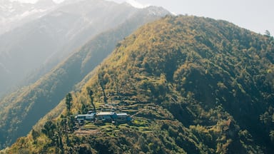 A mountainous landscape with a house and a blue vehicle on a hillside.