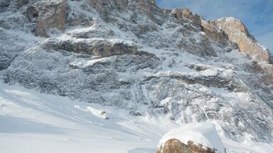A snow-covered mountain with rocky outcrops and a large boulder in the foreground.