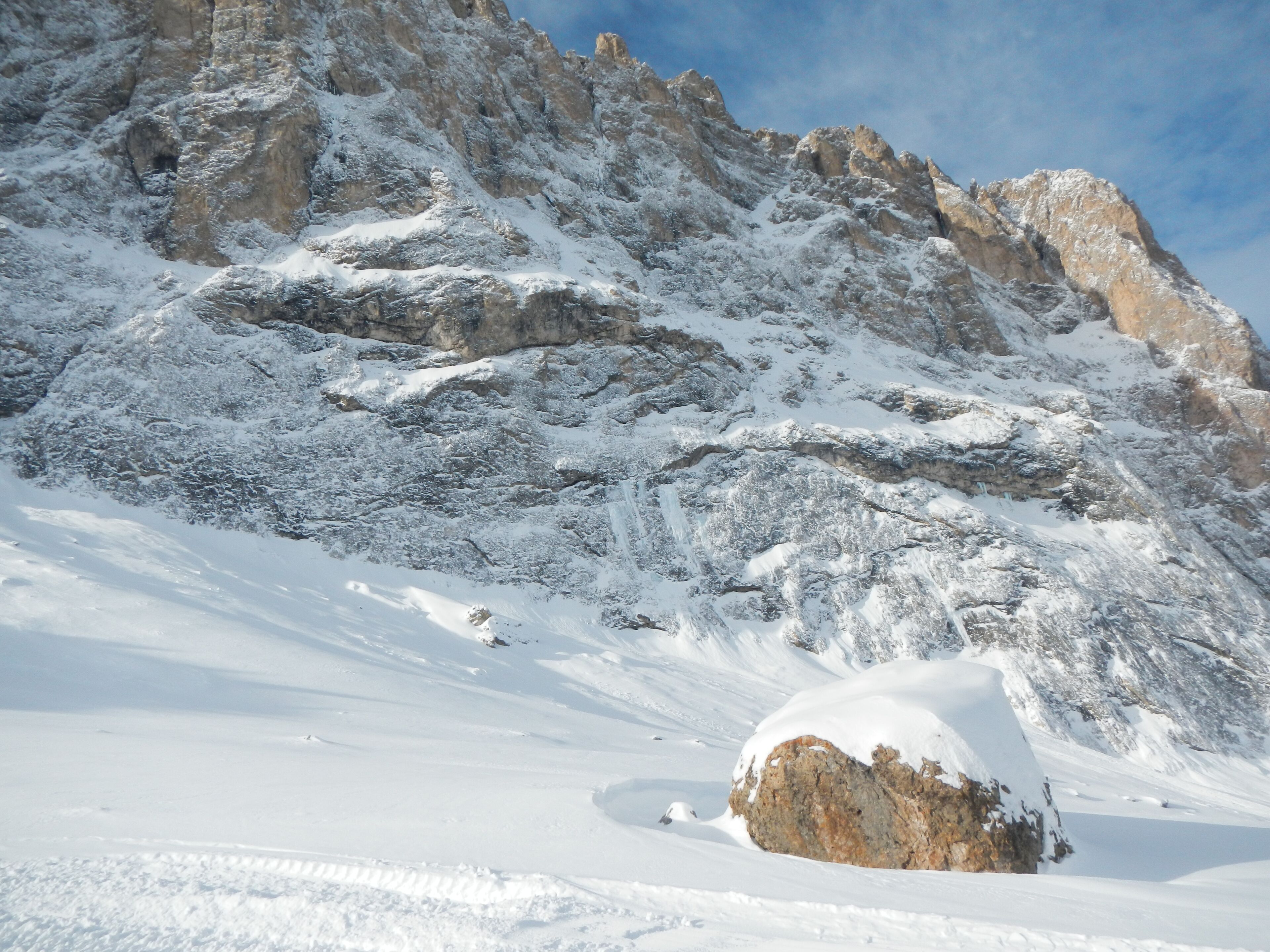 A snow-covered mountain with rocky outcrops and a large boulder in the foreground.