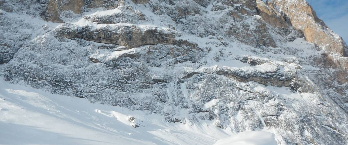A snow-covered mountain with rocky outcrops and a large boulder in the foreground.