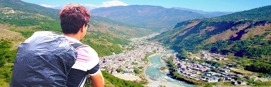 A person overlooking a valley with a river, surrounded by mountains and a small town.