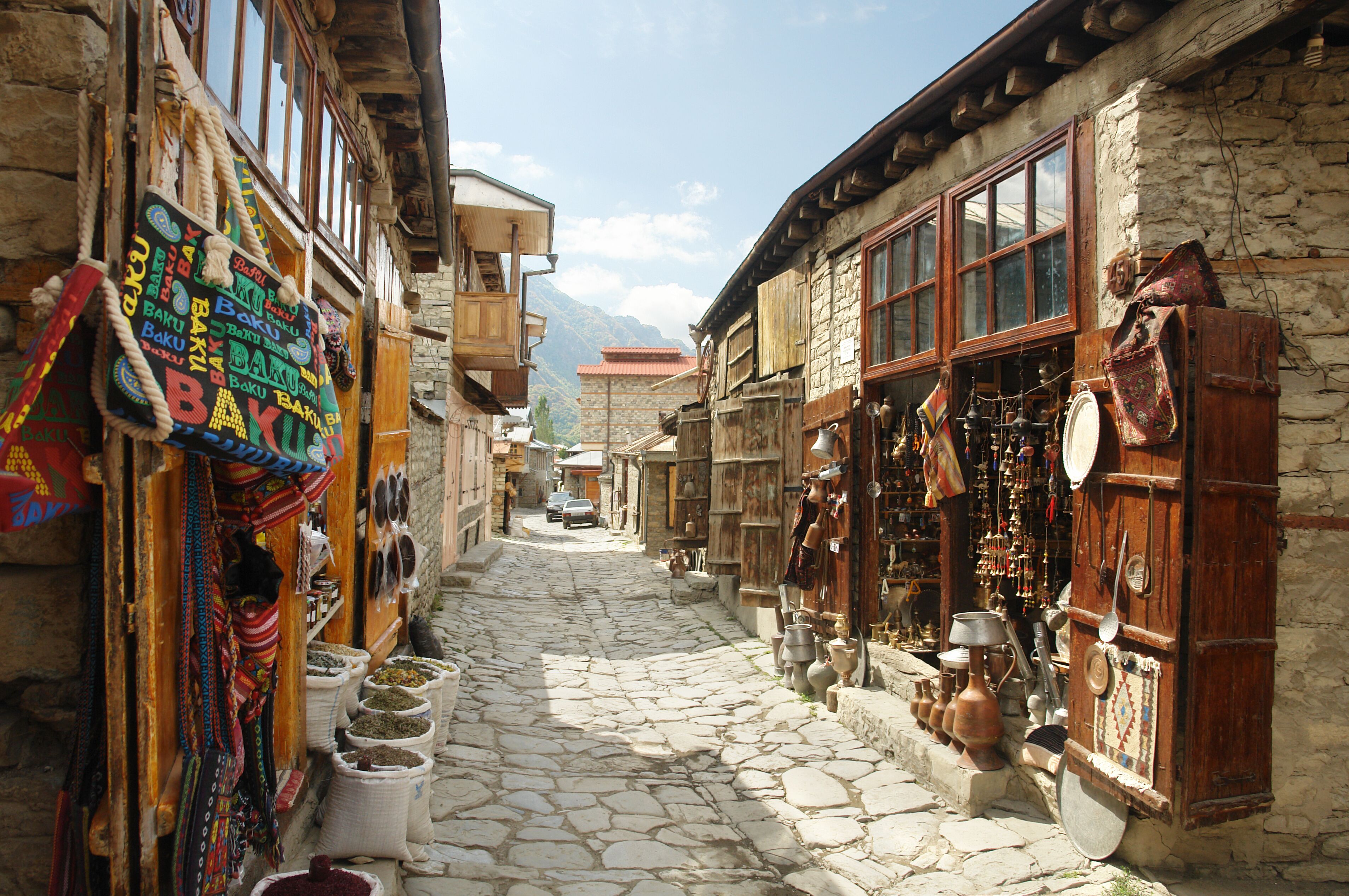 A narrow stone-paved street flanked by traditional buildings with wooden shutters and colorful textiles.