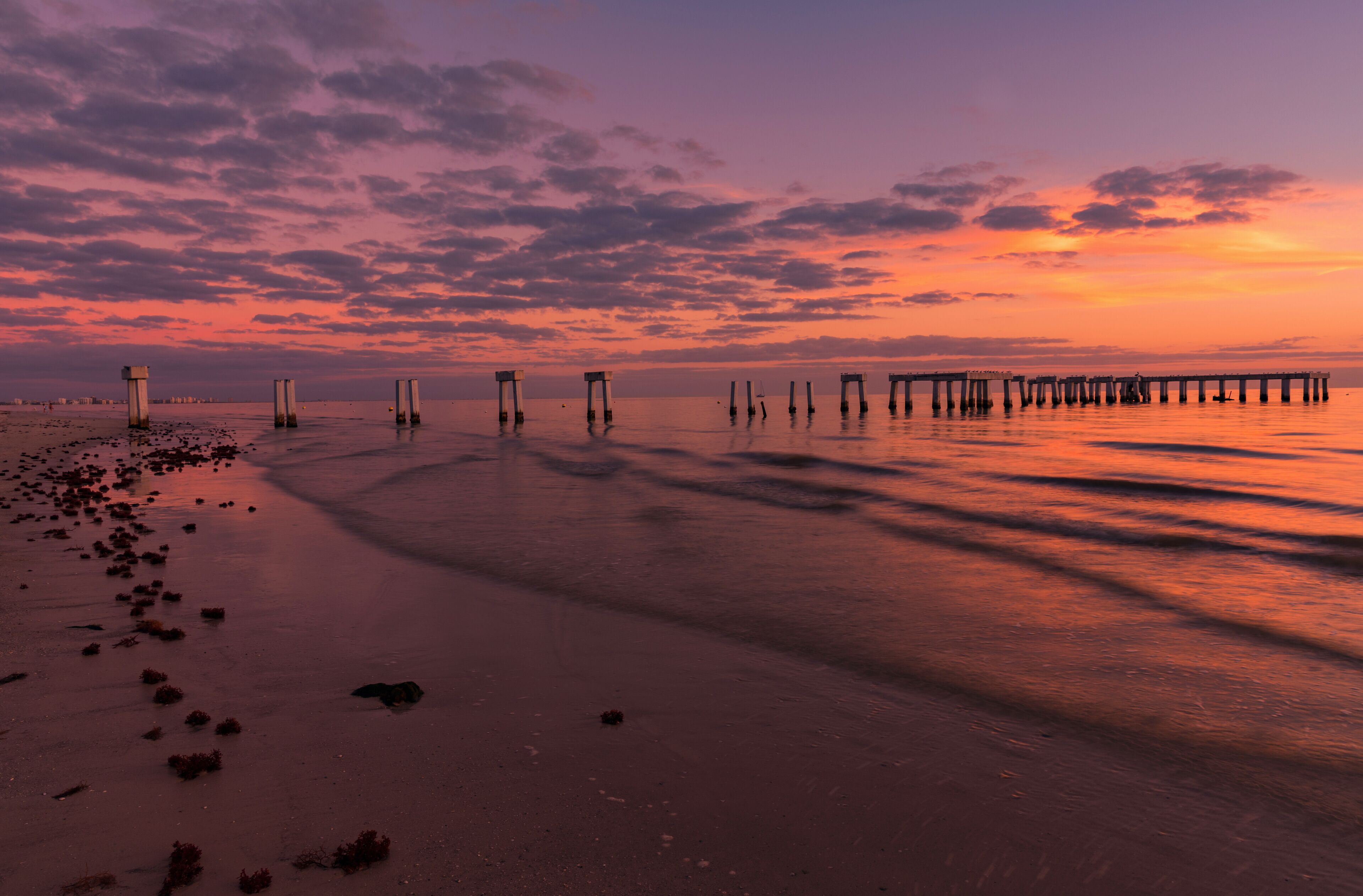 A sunset over a beach with a pier extending into the water.