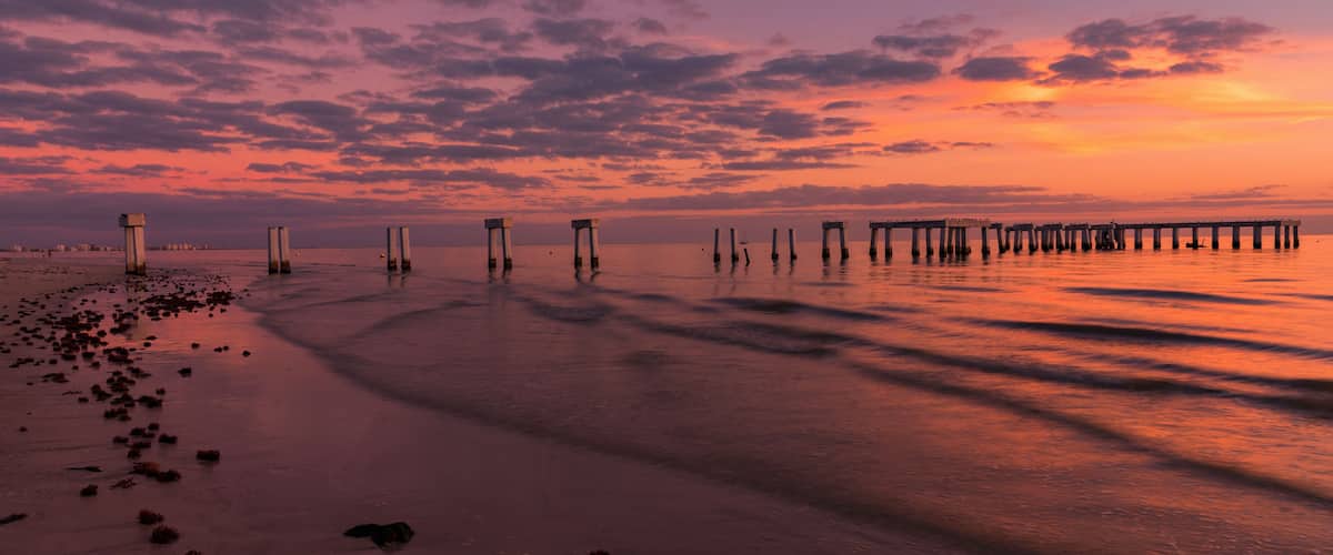 A sunset over a beach with a pier extending into the water.