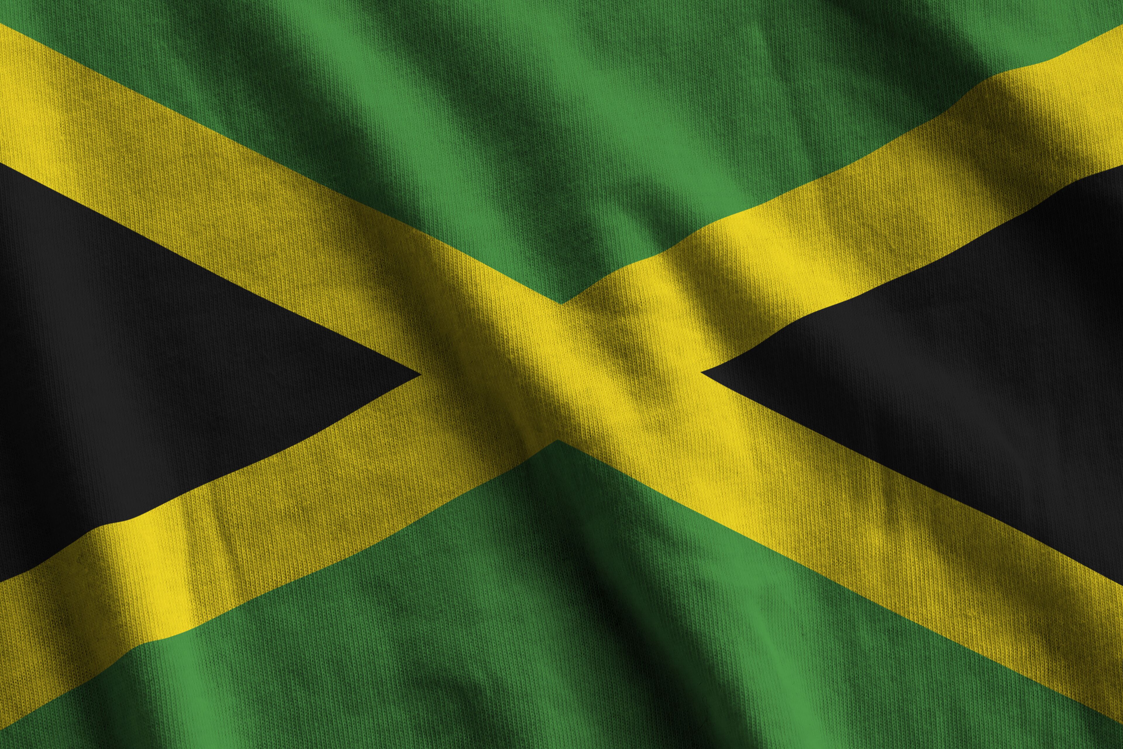 Jamaica flag with big folds waving close up under the studio light indoors. The official symbols and colors in fabric banner