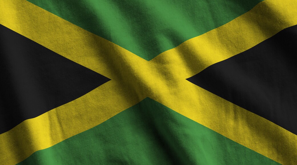 Jamaica flag with big folds waving close up under the studio light indoors. The official symbols and colors in fabric banner